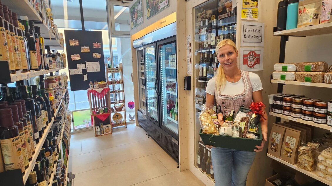 Eine freundliche Frau hält einen Geschenkkorb in einem Lebensmittelladen. Regale voll mit verschiedenen Produkten sind auf beiden Seiten des Ganges sichtbar. | © Verein Schilcherland Spezialtäten