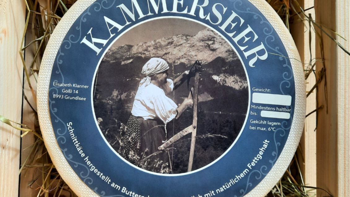Ein runder Käse mit beschriftetem Etikett, das eine Frau beim Käseherstellungsprozess zeigt. Der Käse stammt vom Buttererhof aus Rohmilch und hat eine maximale Lagertemperatur von 6°C. | © Butterer Hofladen