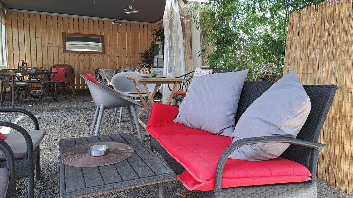Ein gemütlicher Sitzbereich im Freien mit einem roten Sofa und großen Kissen. Im Hintergrund sind Tische und Stühle in einer entspannten Atmosphäre zu sehen. | © TVB_Steininger