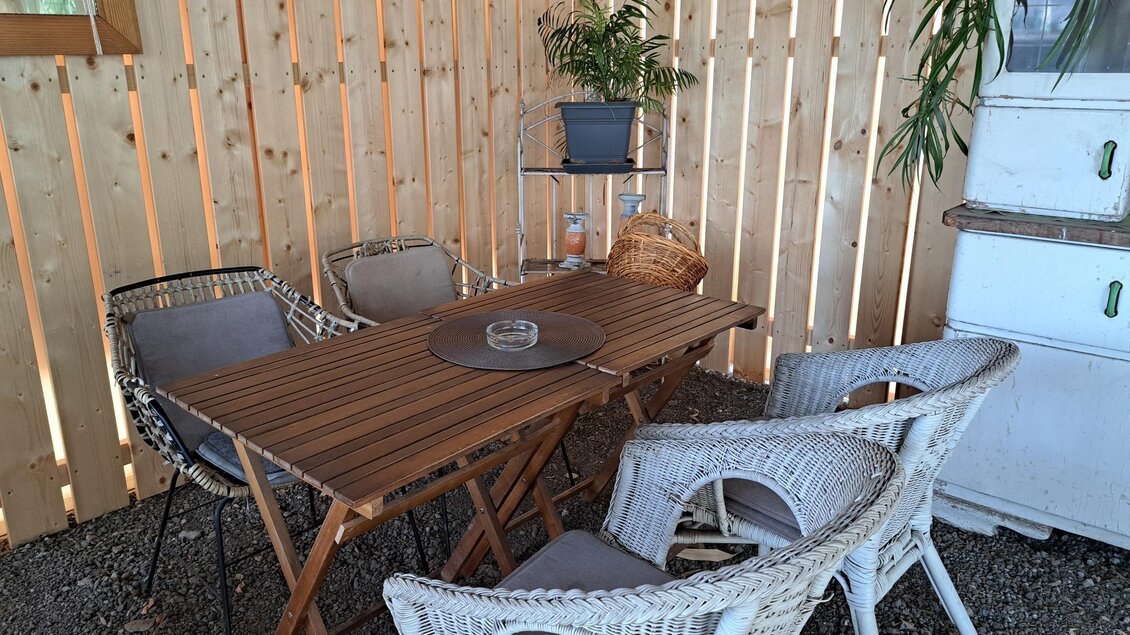 Ein gemütlicher Aufenthaltsbereich mit einem Holztisch und Stühlen aus Rattan. Die Wand besteht aus vertikalen Holzlatten und es sind einige Pflanzen vorhanden. | © TVB_Steininger