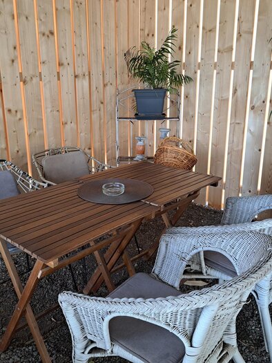 Ein gemütlicher Aufenthaltsbereich mit einem Holztisch und Stühlen aus Rattan. Die Wand besteht aus vertikalen Holzlatten und es sind einige Pflanzen vorhanden. | © TVB_Steininger