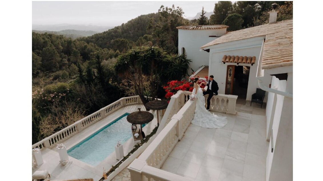 Eine elegante Hochzeitsfeier auf einer Terrasse mit Blick auf eine schöne Landschaft. Im Vordergrund stehen das Brautpaar und ein Pool, umgeben von Blumen. | © Sibel Zechmann Fotografie & Content Creation