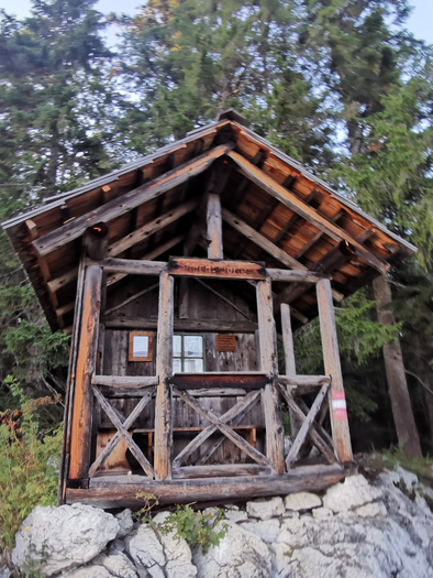 Eine kleine Holzhütte steht auf einem Felsen, umgeben von Bäumen. Die Hütte hat ein rustikales Dach und große Fenster. | © TVB Ausseerland Salzkammergut_Theresa Schwaiger