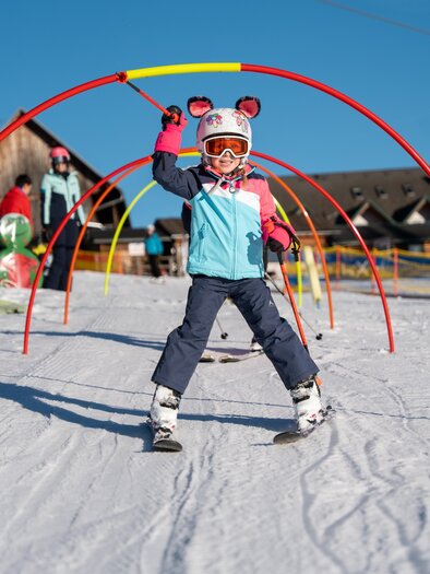 A child is seen skiing, laughing and waving at the camera. | © Cian Baumgartner