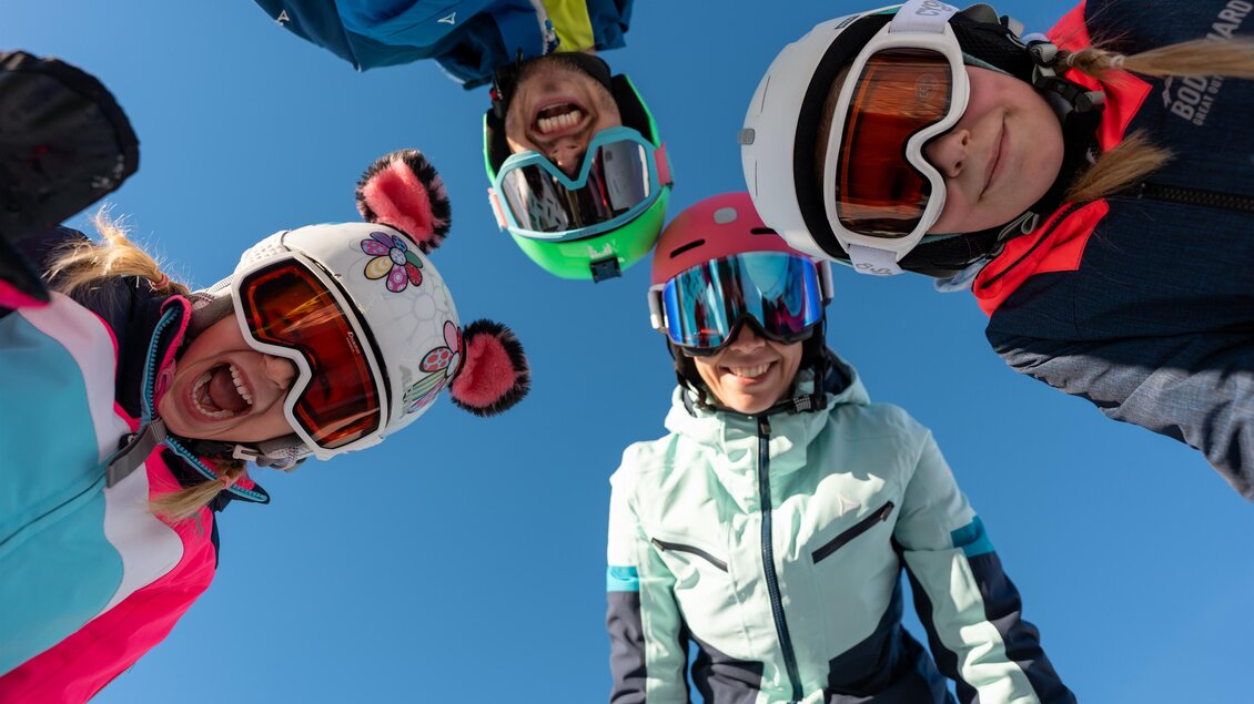 Vier Skifahrerinnen die von oben lachend die die Kamera blicken mit strahlend blauem Himmel im Hintergrund. | © Cian Baumgartner