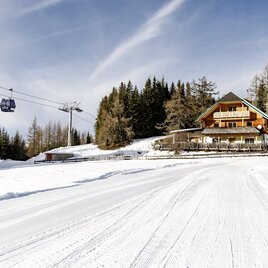 A picturesque mountain cabin in the snowy winter forest. Ski lifts soar over the calm landscape. | © Tourismusverband Murau