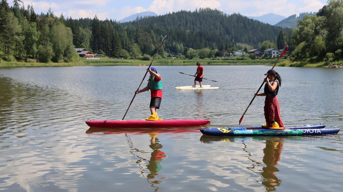 Drei Personen paddeln auf einem ruhigen See. Im Hintergrund sind grüne Wälder und Berge zu sehen. | © TVB Erzberg-Leoben