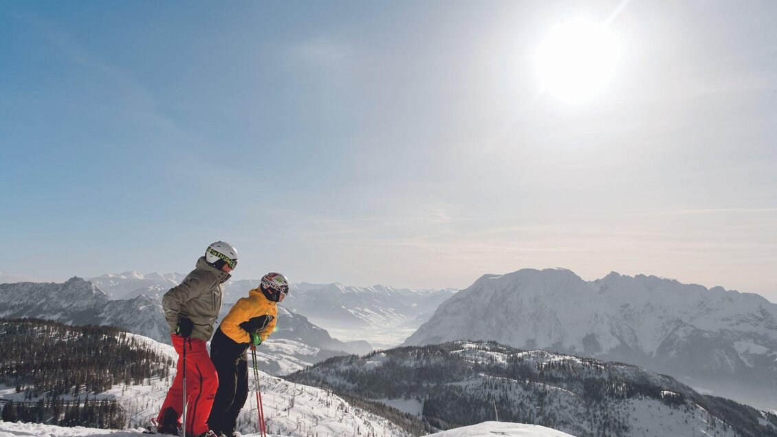<p>Zwei Skifahrer stehen auf der schneebedeckten Tauplitz und genießen die Aussicht auf das Aussseerland mit dem atemberaubenden Grimming. Der Himmel ist blau und die Sonne strahlt hell.</p> | © Aldiana Salzkammergut und GrimmingTherme