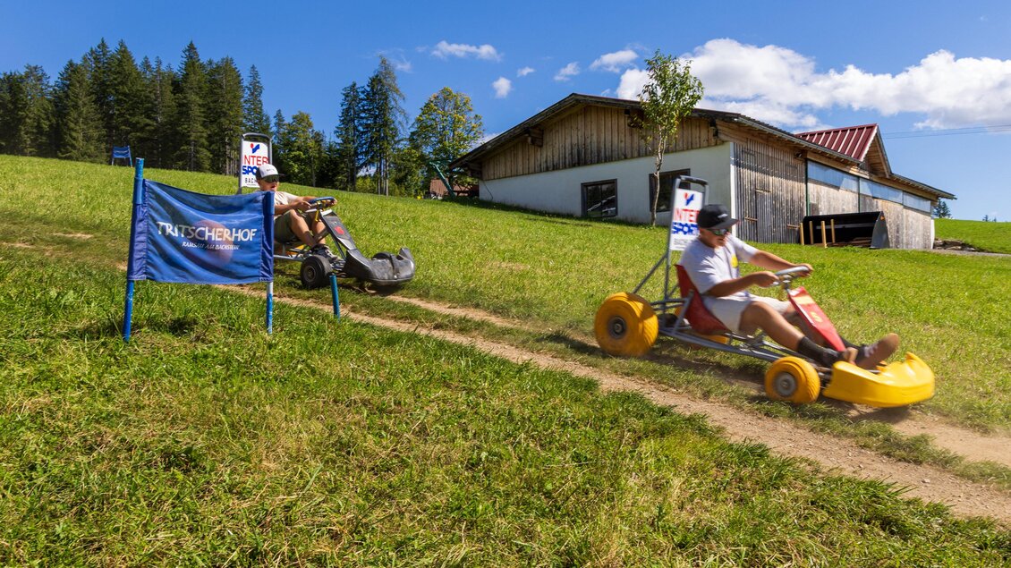 Ein alter Go-Kart auf einer Wiese mit einem blauen Himmel im Hintergrund. Im Bild ist ein Startbanner und ein Haus zu sehen. | © Hans-Peter Steiner