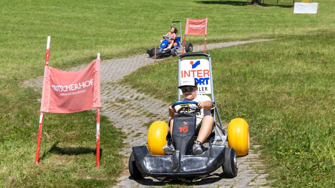 Ein junger Fahrer sitzt in einem Go-Kart auf einem schmalen Weg, umgeben von Grün. Im Hintergrund fährt ein weiterer Teilnehmer ebenfalls in einem Go-Kart. | © Hans-Peter Steiner