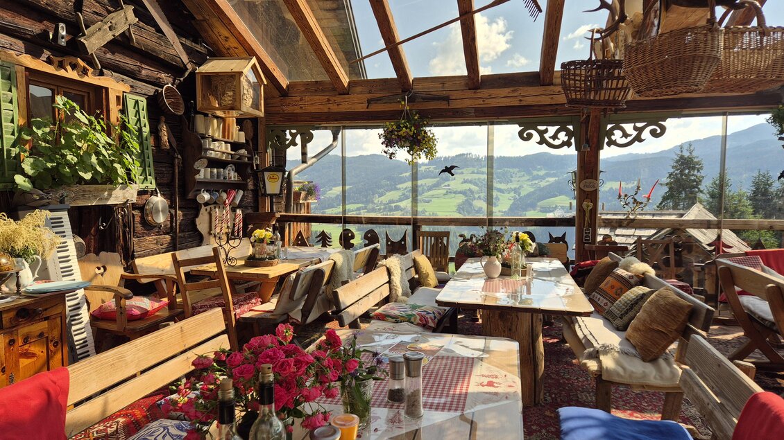 Ein gemütliches Restaurant mit rustikalem Holzdekor und Blick auf eine idyllische Berglandschaft. Der Tisch ist mit Blumen und bunten Kissen dekoriert. | © TV Murau