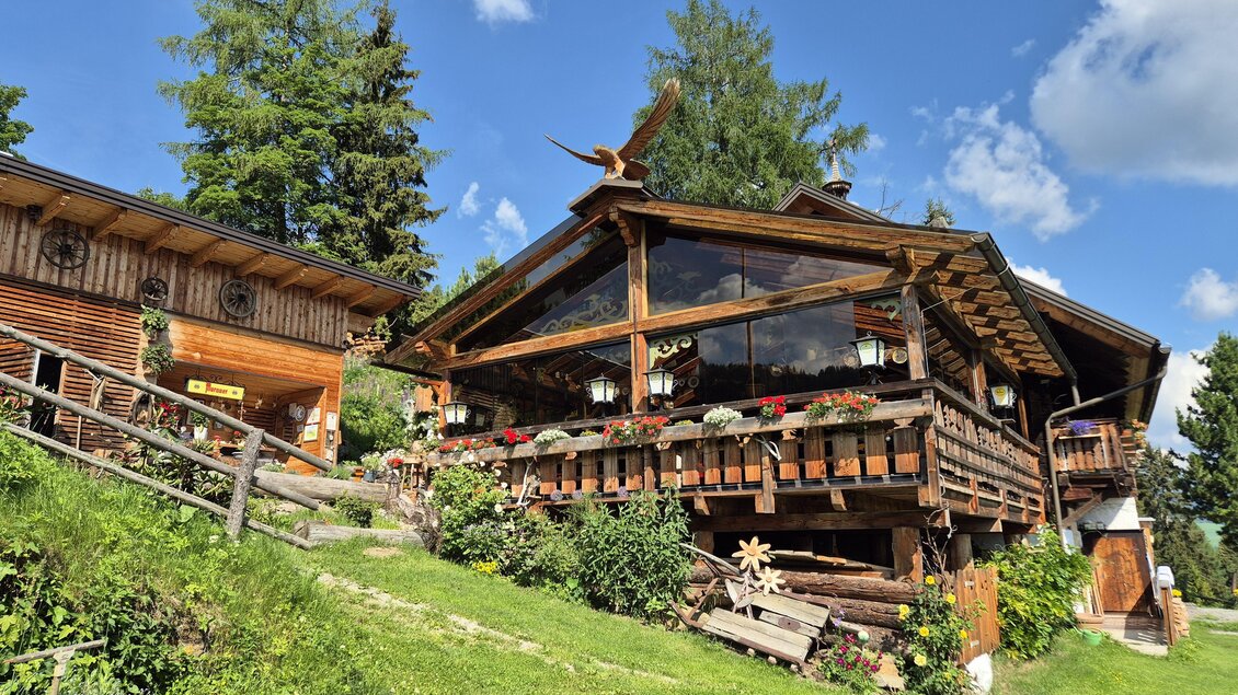 Ein traditionelles Holzhaus umgeben von üppigem Grün und hohen Bäumen. Der klare Himmel ergänzt die idyllische Atmosphäre. | © TV Murau
