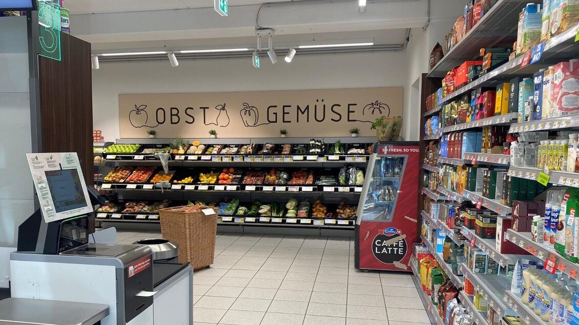 Ein Supermarktbereich mit frischem Obst und Gemüse. Regal mit verschiedenen Lebensmitteln und einem Selbstbedienungskiosk im Vordergrund. | © Bettina Scheck