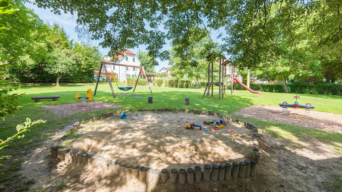 Ein Spielplatz mit einer Sandkiste, Schaukeln und Rutschen. Der Bereich ist von Bäumen umgeben und lädt zum Spielen ein. | © Helmut Schweighofer