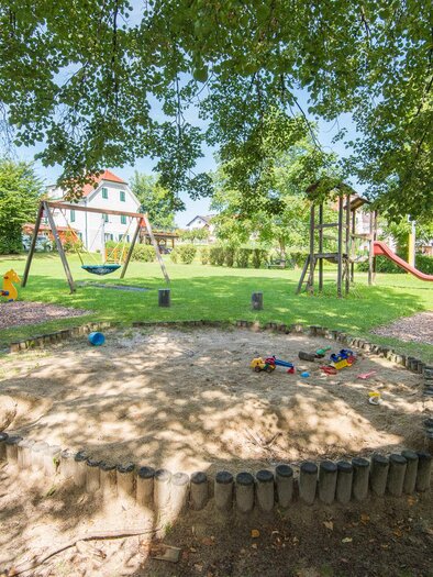 A playground with a sandpit, swings, and slides. The area is surrounded by trees and invites play. | © Helmut Schweighofer