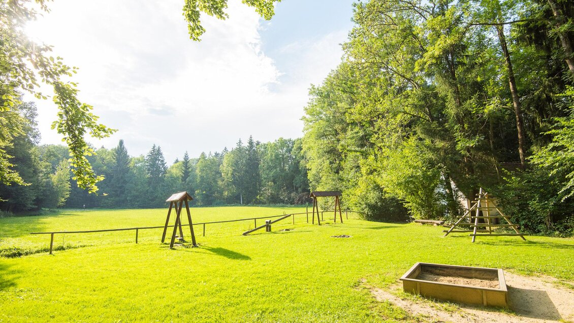 Ein schöner Spielplatz in einer grünen Wiese, umgeben von Bäumen. Im Hintergrund sind Schaukeln und ein Spielbereich zu sehen. | © Helmut Schweighofer