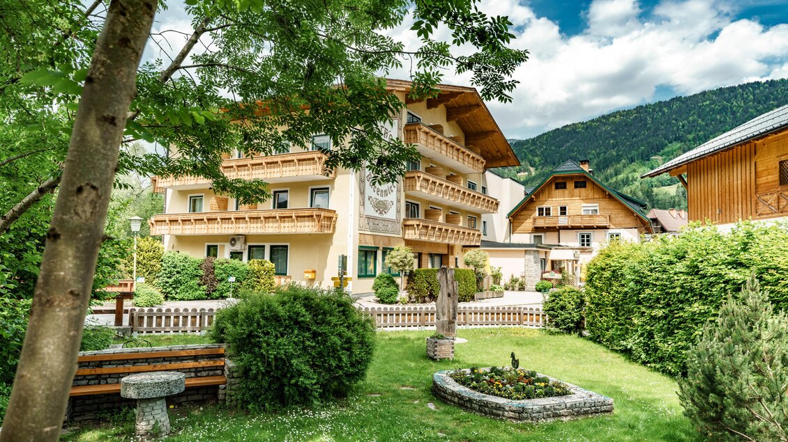 Ein charmantes Gebäude mit Balkonen, umgeben von einem gepflegten Garten. Im Hintergrund sind sanfte Hügel und ein blauer Himmel zu sehen. | © Bärenwirt