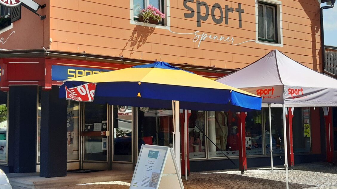 Ein Sportgeschäft mit einem großen Eingang und bunten Sonnenschirmen vor der Tür. Oben ist das Schild mit dem Schriftzug "Sport Spanker" zu sehen. | © TVB Ausseerland Salzkammergut/Raunigg