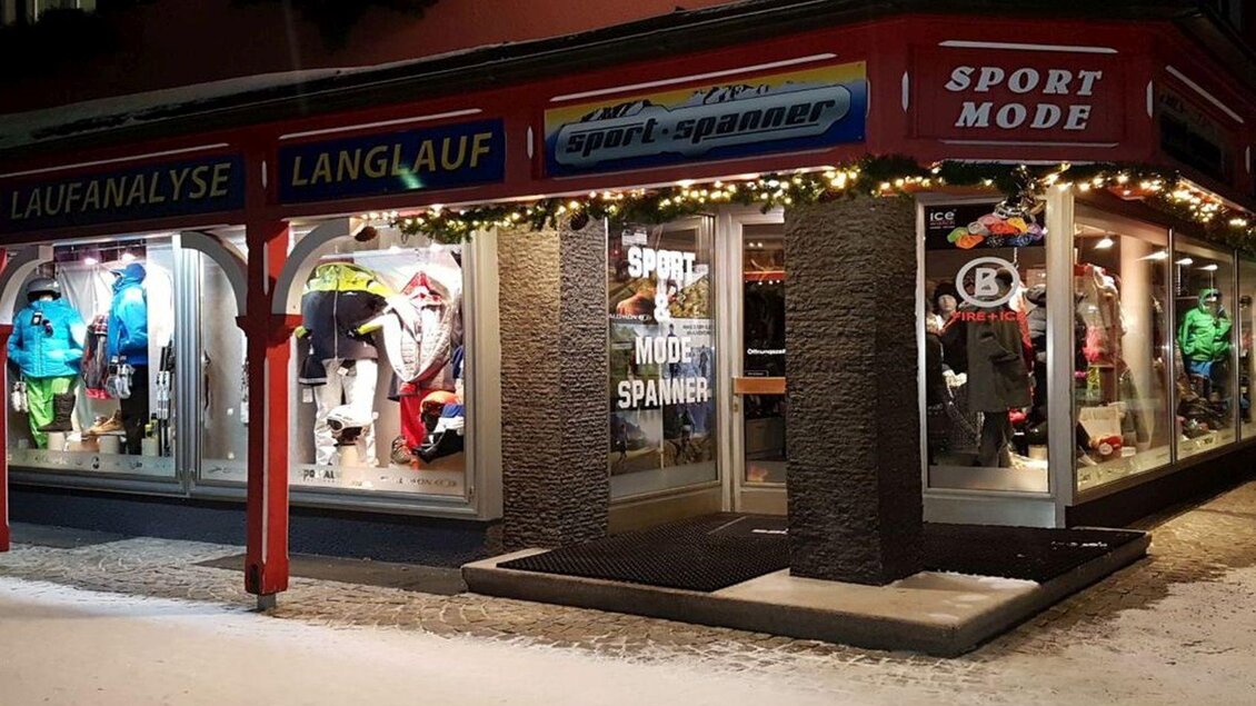 Ein sportlicher Geschäftsbereich mit bunten Sportkleidungen in den Schaufenstern. Die Fassade ist festlich beleuchtet und es gibt Hinweise auf Laufanalyse und Langlaufangebote. | © Sport Spanner