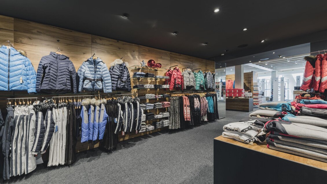 Ein moderner Bekleidungsladen, der verschiedene Jacken und Wollpullover ausstellt. Die Wände sind mit mehreren Kleidungstücken in kühlen Farben dekoriert. | © Sport Tritscher Rohrmoos