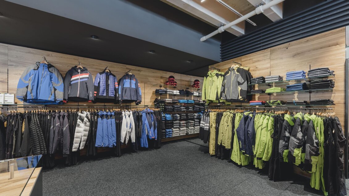 Ein moderner Bekleidungsladen mit einer Auswahl an Jacken und Sportbekleidung. Die Wände sind mit Regalen gefüllt, die verschiedene Farben und Stile zeigen. | © Sport Tritscher Shop in Rohrmoos