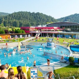 Ein großer Schwimmbereich mit vielen Menschen und einem Rutschenbereich im Freizeitpark Frohnleiten. Im Hintergrund sind grüne Hügel und ein modernes Gebäude zu sehen. | © TV Region Graz - Rene Vidalli