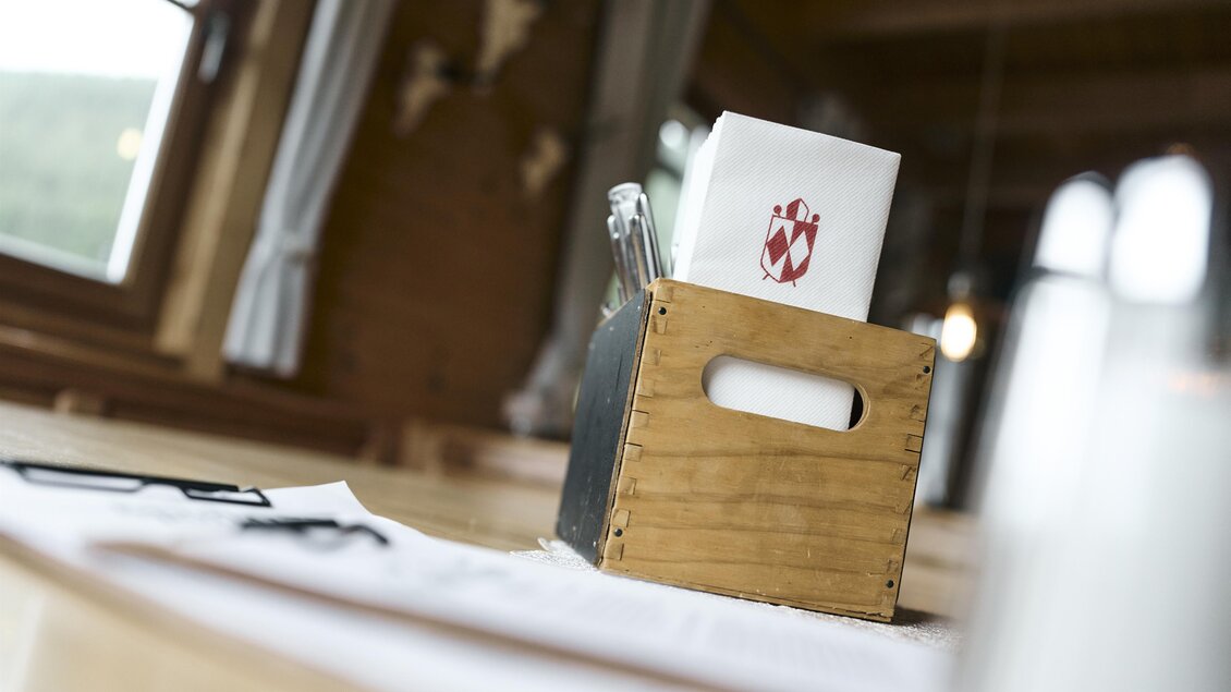 Ein Holzkasten mit Stiften und einem weißen Blatt Papier steht auf einem Tisch. Im Hintergrund sind Fenster und eine rustikale Einrichtung zu sehen. | © Nationalpark Gesäuse
