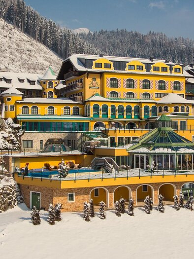 A picturesque hotel building on a hill, surrounded by a snowy landscape. | © Hotel Pichlmayrgut