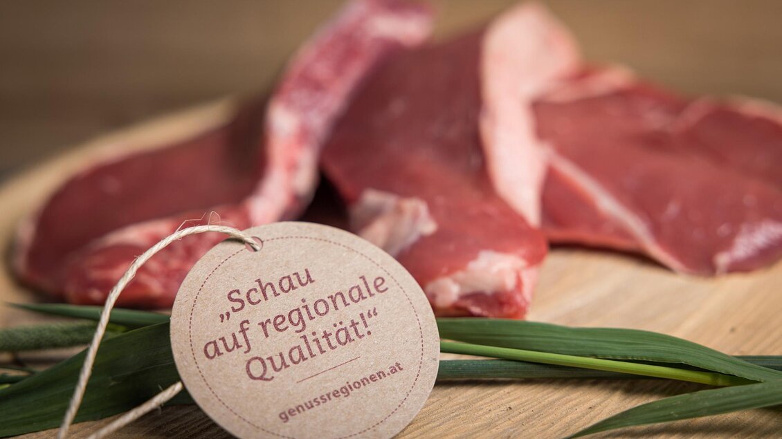 Frisches Fleisch auf einem Holzbrett mit einem Etikett, das zur regionalen Qualität auffordert. Die Präsentation betont die Frische und Herkunft der Produkte. | © Netzwerk Kulinarik wildbild