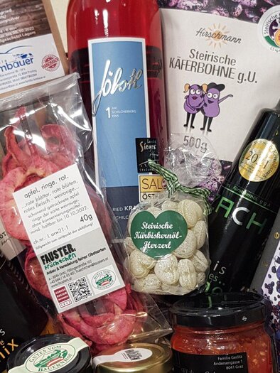 A gift basket with a selection of regional foods and beverages. Contains bottles, snacks, and delicacies arranged in a carefully organized layout. | © Mach Genussprodukte GmbH - Julia Trenker