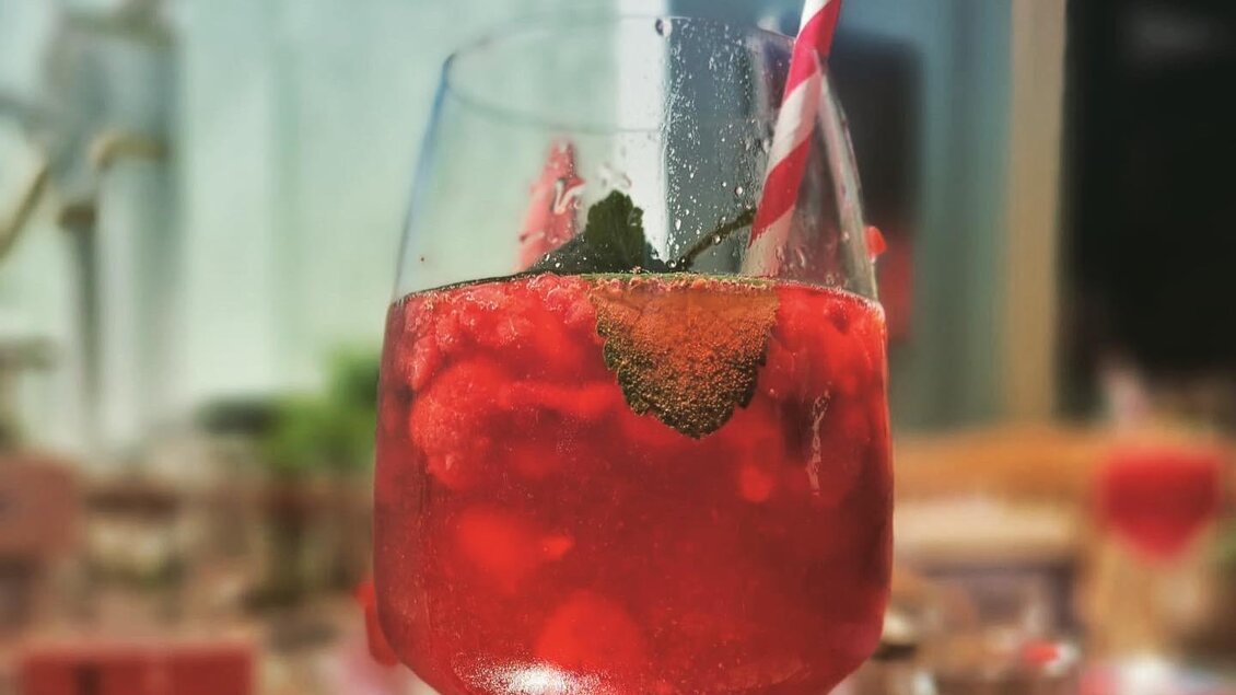  Roter Cocktail mit Eiswürfeln, Beeren, Minze und Trinkhalm in einem Glas im Stadtcafé Voitsberg. | © Stadtcafé VO-Uhl