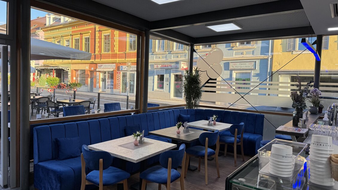 Ein modernes Restaurant mit blauen Sitzbänken und Tischen. Der Raum hat große Fenster und einen Blick auf bunte Häuser draußen. | © Mesut Tunc, Stadtcafe