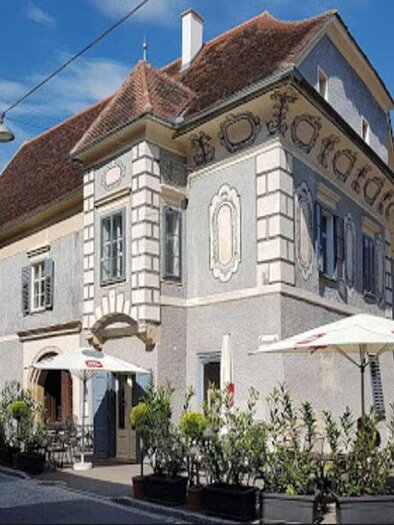 Ein historisches Gebäude mit schöner Architektur in einer Stadt. Draußen stehen Tische und Stühle unter Sonnenschirmen. | © http://tuerkenloch.at/de/