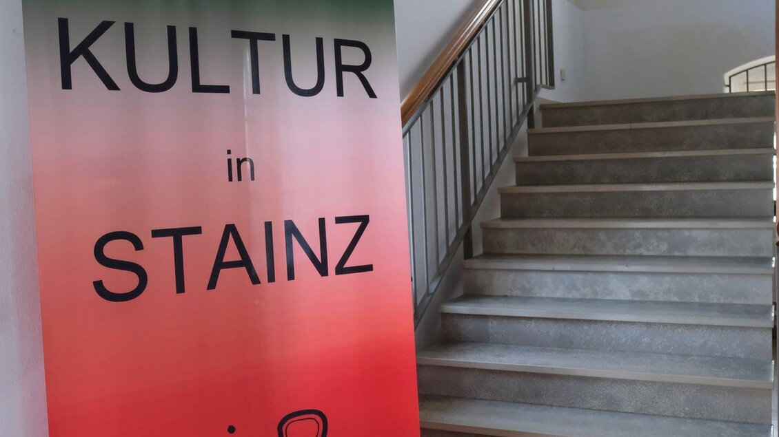 Ein Werbeschild für kulturelle Veranstaltungen in Stainz steht an einer Treppe. Das Schild ist in leuchtenden Farben gehalten und hebt den Text "KULTUR in STAINZ" hervor. | © Helmut Fladenhofer