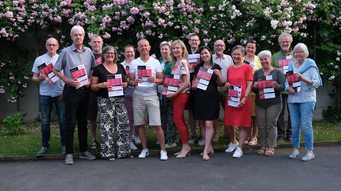 Eine Gruppe von Menschen steht mit Büchern in der Hand vor einer blühenden Hecke. Sie lächeln und posieren für das Foto. | © Helmut Fladenhofer