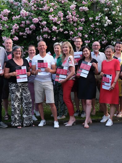 Eine Gruppe von Menschen steht mit Büchern in der Hand vor einer blühenden Hecke. Sie lächeln und posieren für das Foto. | © Helmut Fladenhofer