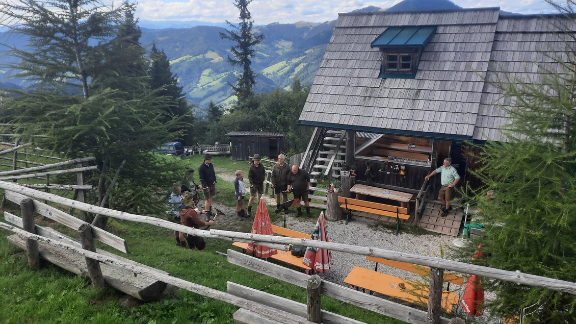Eine Berghütte umgeben von Bäumen und Wiesen. Gruppen von Menschen genießen die frische Luft und die Aussicht. | © Stoahandhütte