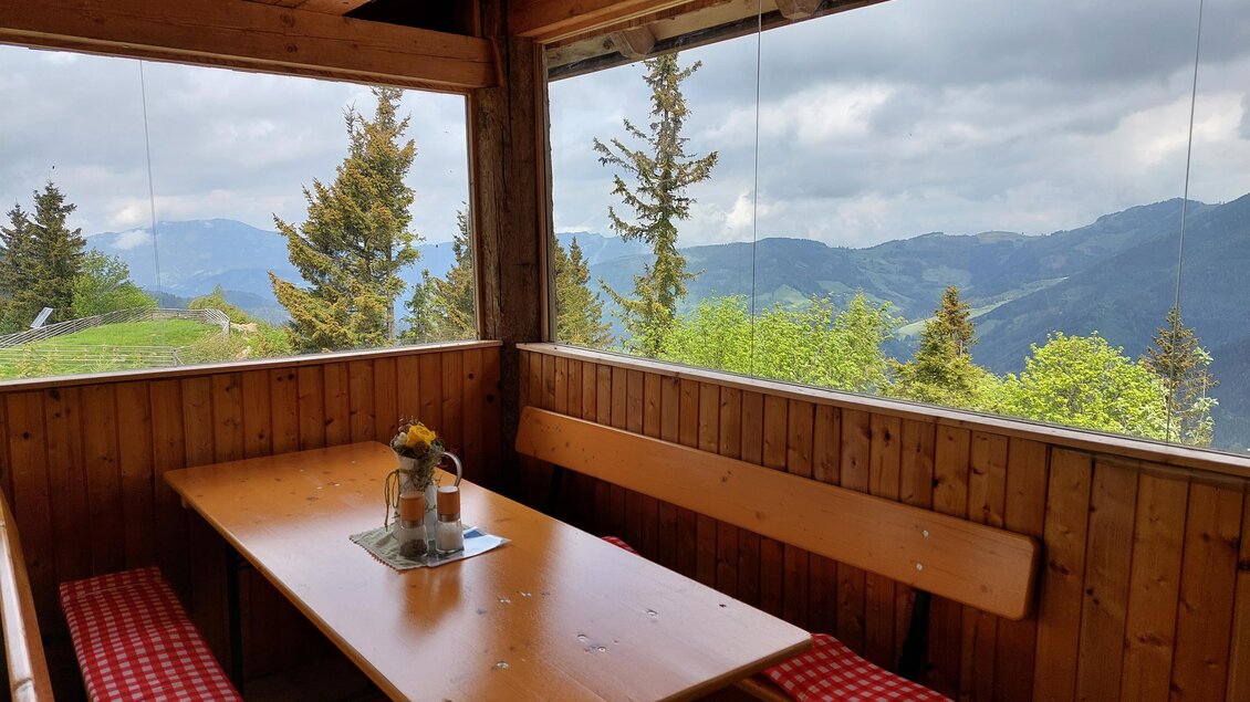 Eine gemütliche Almhütte mit Holzinterieur und Blick auf die Berge. Der Tisch ist gedeckt und es gibt gemütliche Sitzbänke. | © Stoahandhütte