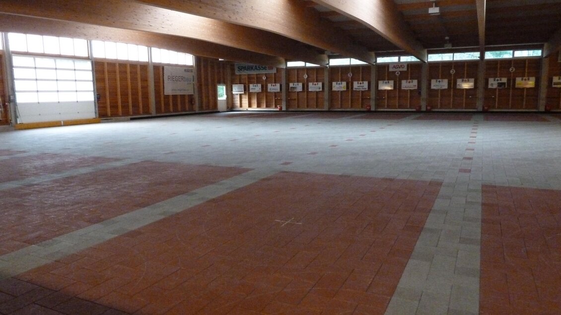 Ein großer, leerer Raum mit Holzdecken und Fenstern. Der Boden ist teilweise mit grauen und roten Fliesen bedeckt. | © POSS-Zentrum