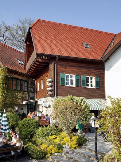 Ein gemütliches Restaurant mit traditionellen Gebäuden und einem schönen Außenbereich. Gäste sitzen entspannt im Freien unter Bäumen. | © Stoffbauer