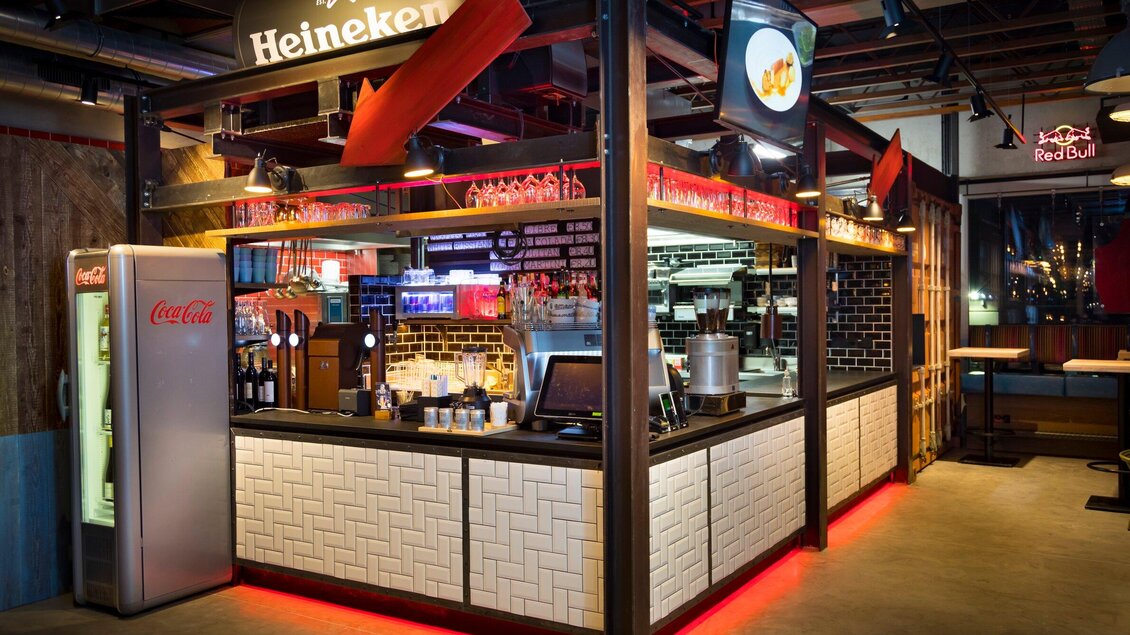 Eine moderne Bar mit einem Heineken-Schild und einer Vielzahl von Getränken. Der Bereich ist stilvoll eingerichtet mit einer beleuchteten Bar und Industriedesign. | © Streets - Werner Krug