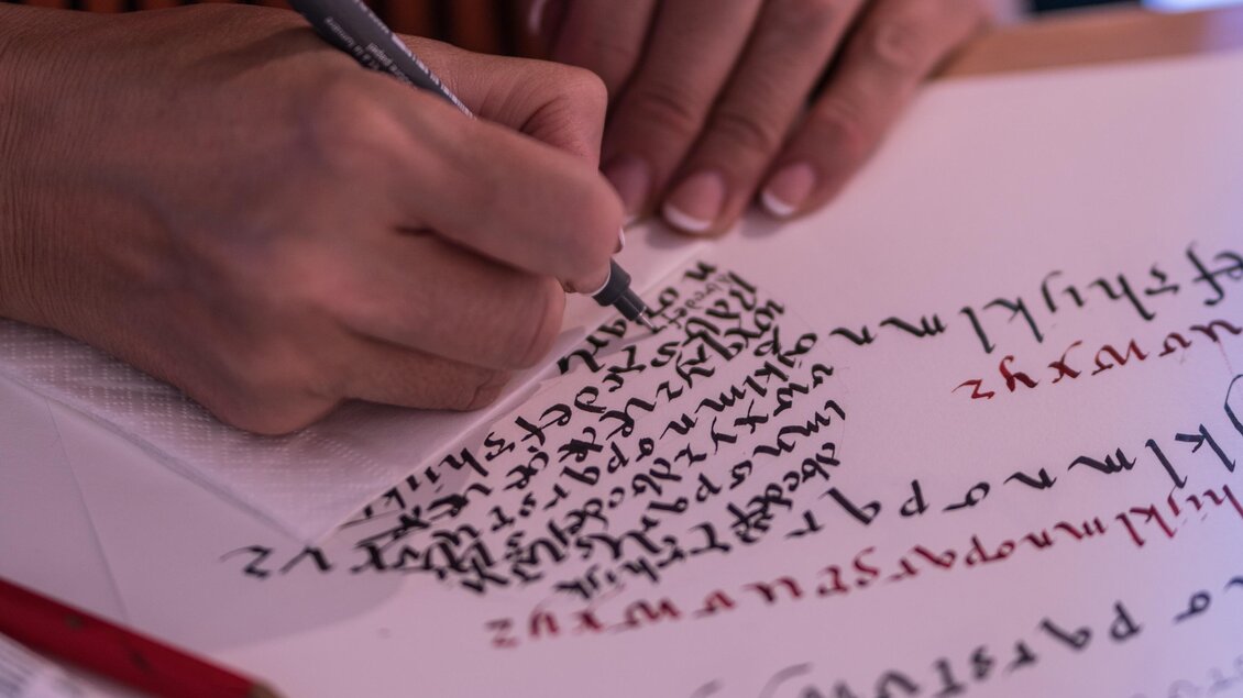 Eine Person schreibt mit einem schwarzen Stift auf ein Blatt Papier. Die Schrift ist künstlerisch und geschwungen. | © Christian Strassegger