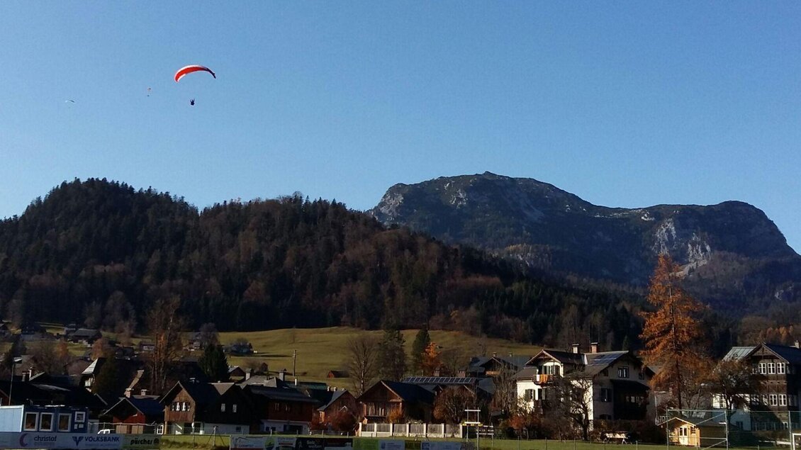 <p>Ein Gleitschirmflieger schwebt über das malerische Ausseerland. Im Hintergrund sind die Berge der Region und mehrere Häuser zu sehen.</p> | © Petra Kirchschlager