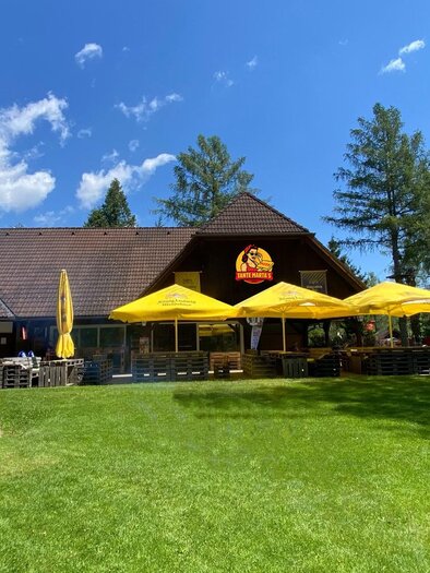Ein Gebäude mit einem großen Garten und mehreren gelben Sonnenschirmen. Die Atmosphäre ist hell und einladend, umgeben von Bäumen und blauem Himmel. | © Oststeiermark Tourismus
