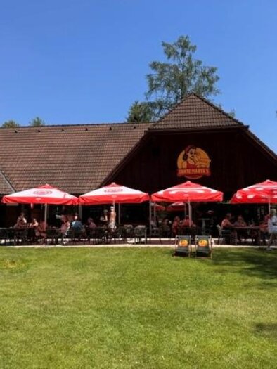 Ein Gebäude mit einem großen Garten und mehreren gelben Sonnenschirmen. Die Atmosphäre ist hell und einladend, umgeben von Bäumen und blauem Himmel. | © Oststeiermark Tourismus
