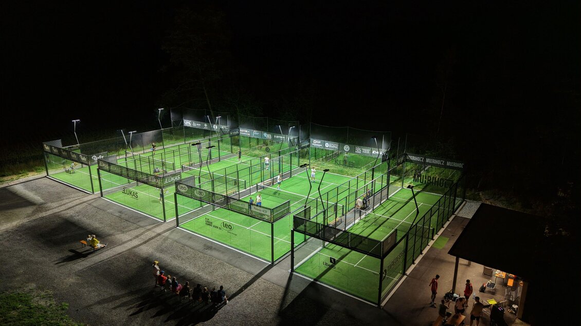 Eine moderne Sportanlage bei Nacht mit beleuchteten Padelplätzen. Menschen stehen in der Nähe und genießen die Atmosphäre. | © Matthias Pignitter