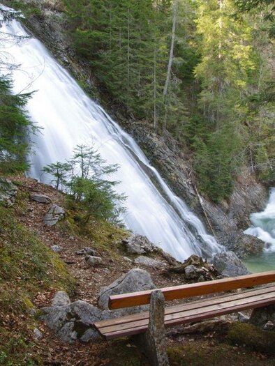 <p>The picturesque Tauplitz waterfall surrounded by lush greenery and tall trees. A wooden bench invites you to linger and enjoy nature.</p> | © Robert Seebacher