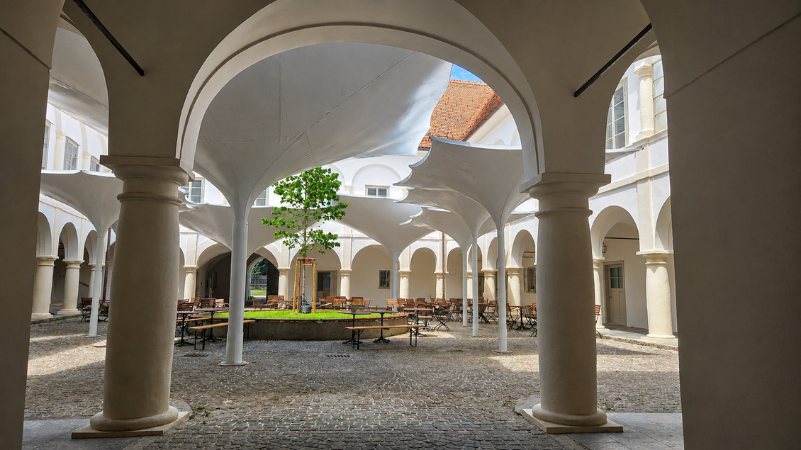 Ein Innenhof mit hohen Säulen und modernen Überdachungen. In der Mitte steht ein kleiner Baum und es gibt Tische und Stühle für Gäste. | © Schloss Retzhof