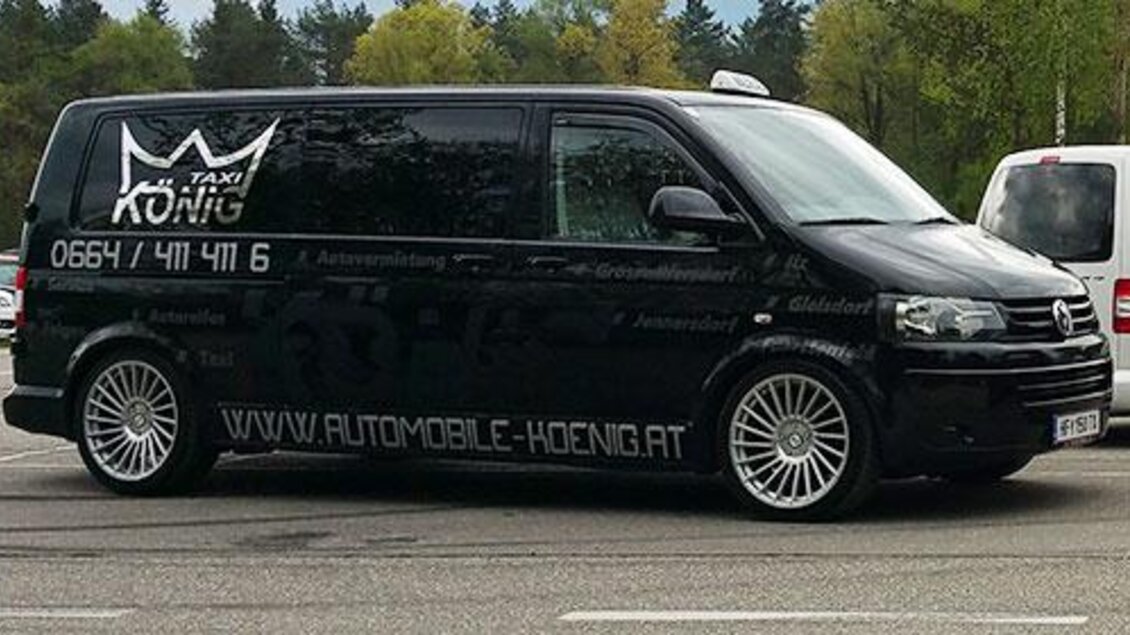 Ein schwarzes Taxi mit dem Namen "König" steht auf einem Parkplatz. Es hat auffällige Felgen und Kontaktinformationen an der Seite.