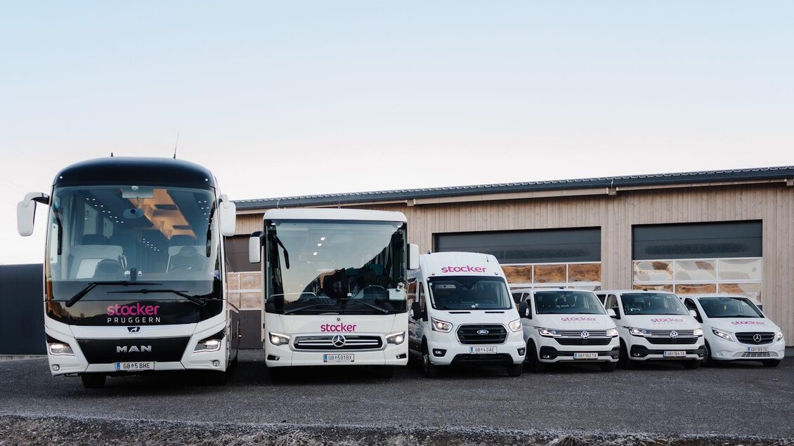 Eine Flotte von Fahrzeugen steht vor einem Gebäude. Die Reihe umfasst Busse und Nutzfahrzeuge mit dem Logo „stocker“. | © Stocker Reisen
